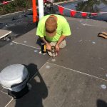 An Eckstein Roofing technician kneeling on a commercial flat roof deck, driving mechanical fasteners through high-density insulation boards during a Storm Damage Roof Repair Cincinnati OH intervention.