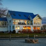 A custom modern coastal home featuring a vibrant blue standing seam system, illustrating a high-performance alternative in the Metal vs Asphalt Roofing comparison by Eckstein Roofing Co.